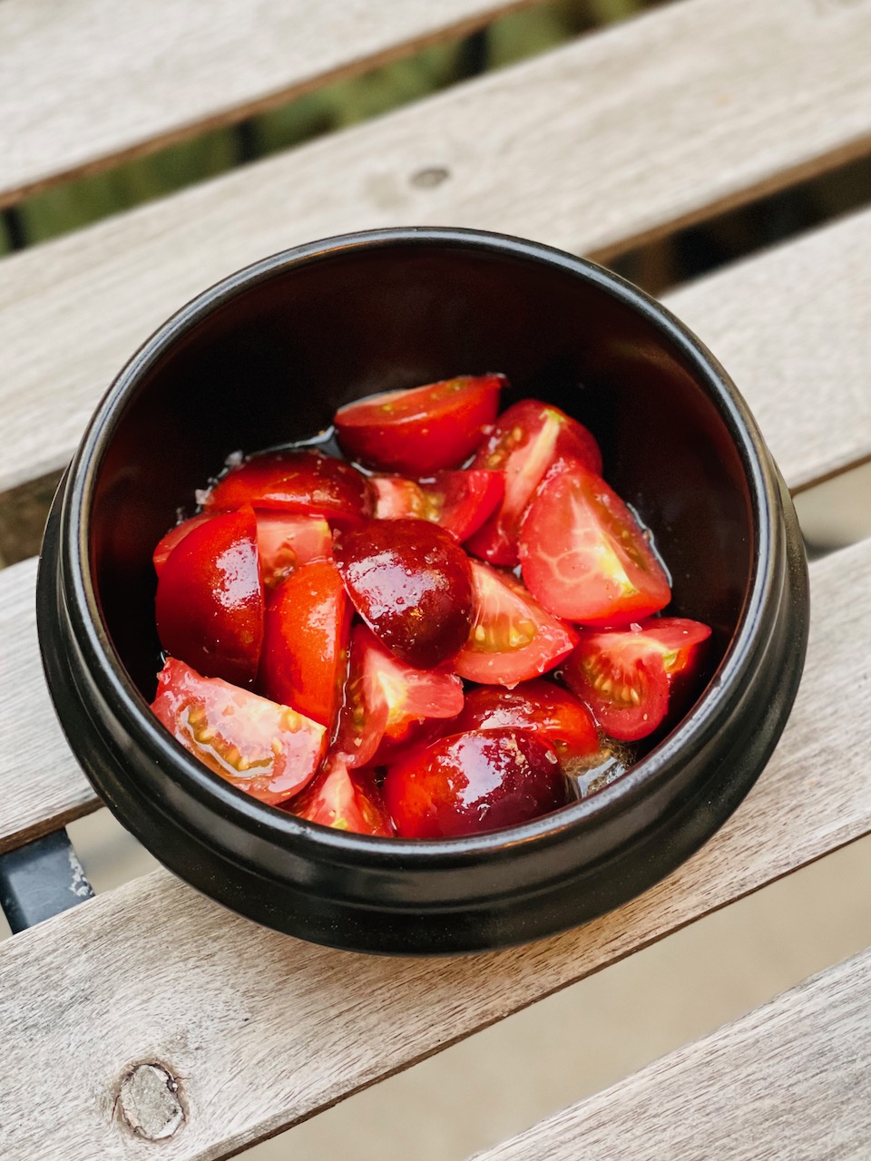 Photo of a dark bowl containing cut tomatoes made very glossy by olive oil.