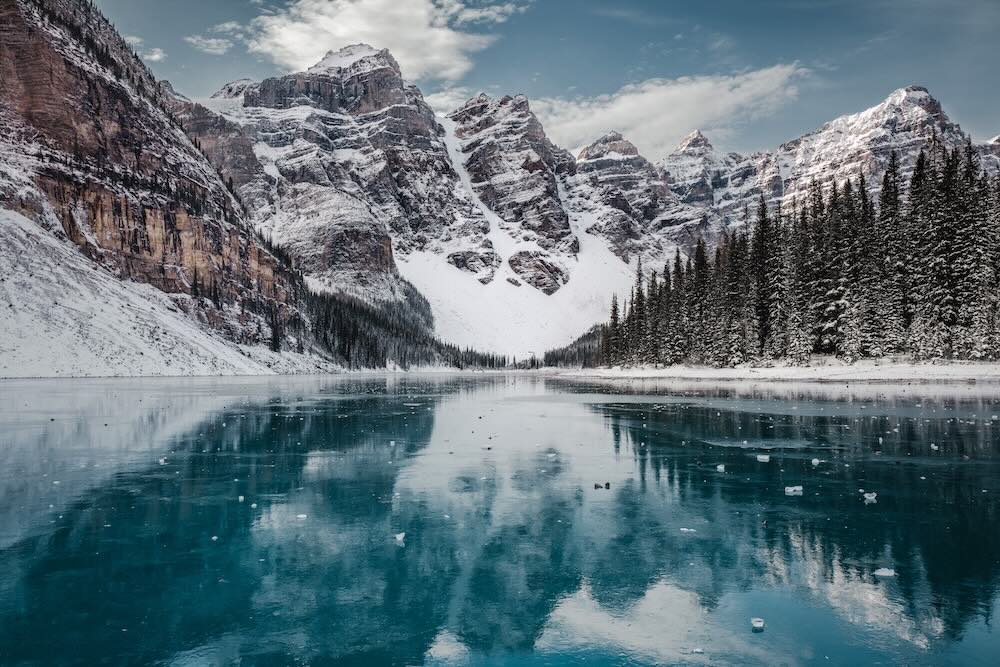 A photo of Moraine Lake, Alberta, frozen with chunks of ice and rocks on its surface.